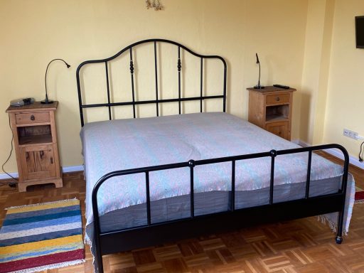 Schlafzimmer mit einem Metallbett, Holzmöbeln und einem bunten Teppich.