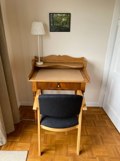 Arbeitsplatz Holztisch mit Stuhl, Schreibtischlampe und Wandbild in einem hellen Raum.