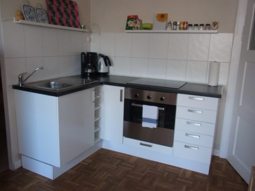 Moderne Küche mit weißen Schränken, schwarzer Arbeitsplatte und Edelstahlgeräten.